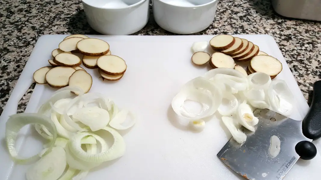 sliced potatoes, a knife, and sliced onions on a cutting board.