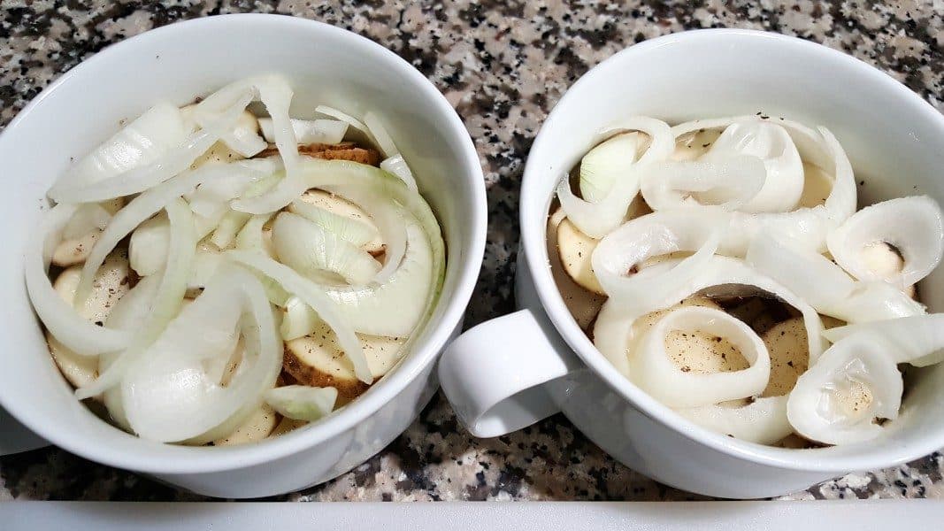 two bowls filled with sliced potatoes topped with sliced onions
