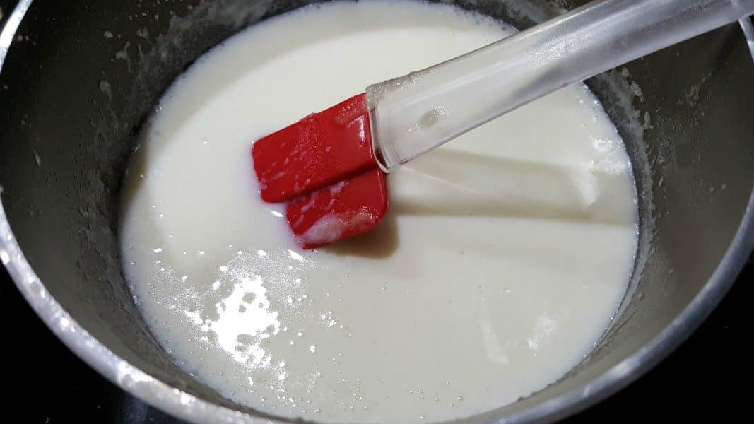 a white sauce and red spatula in a sauce pan
