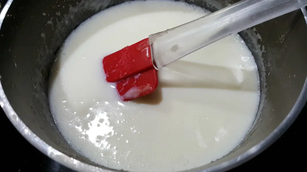a white sauce and red spatula in a sauce pan.