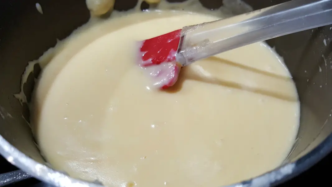 a creamy au gratin cheese sauce and red spatula in a sauce pan.