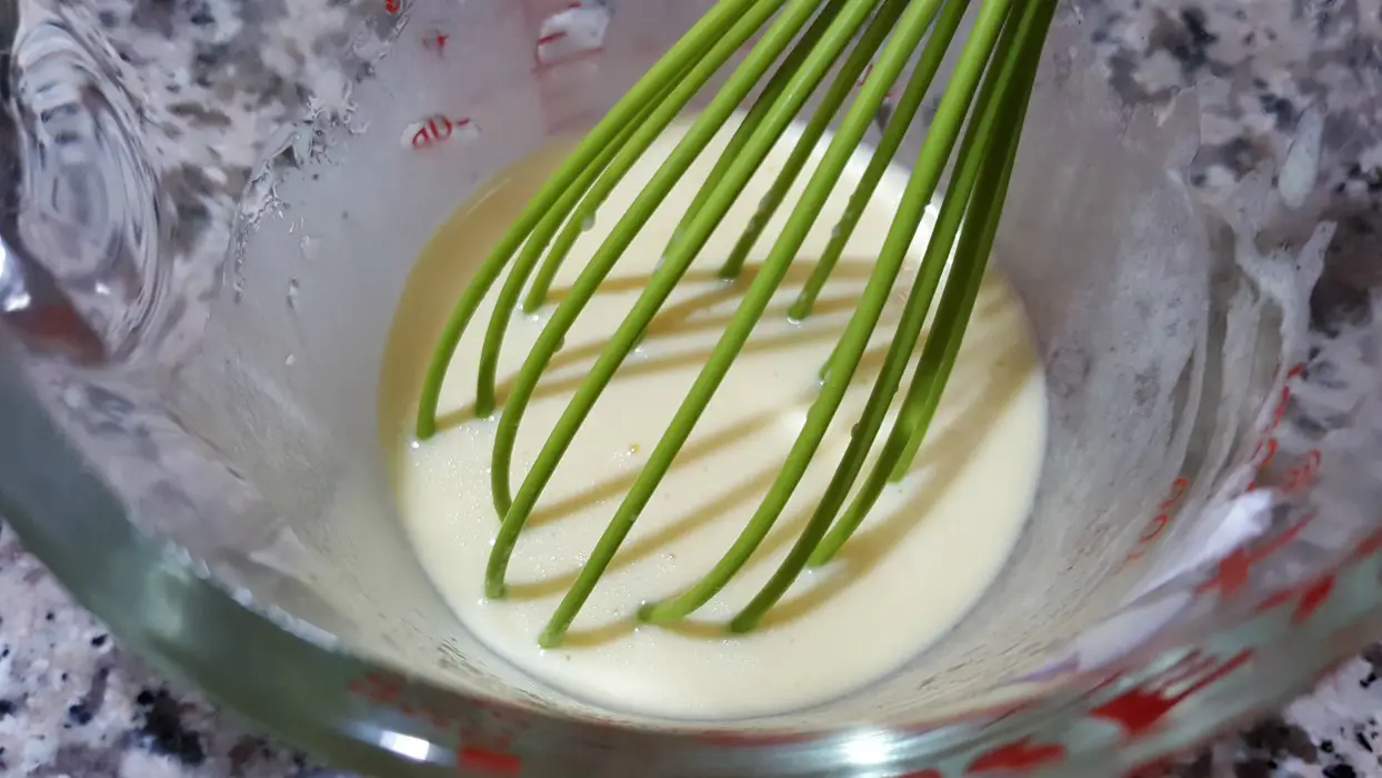 egg, sour cream, oil and almond extract mixed together in a bowl with a whisk.