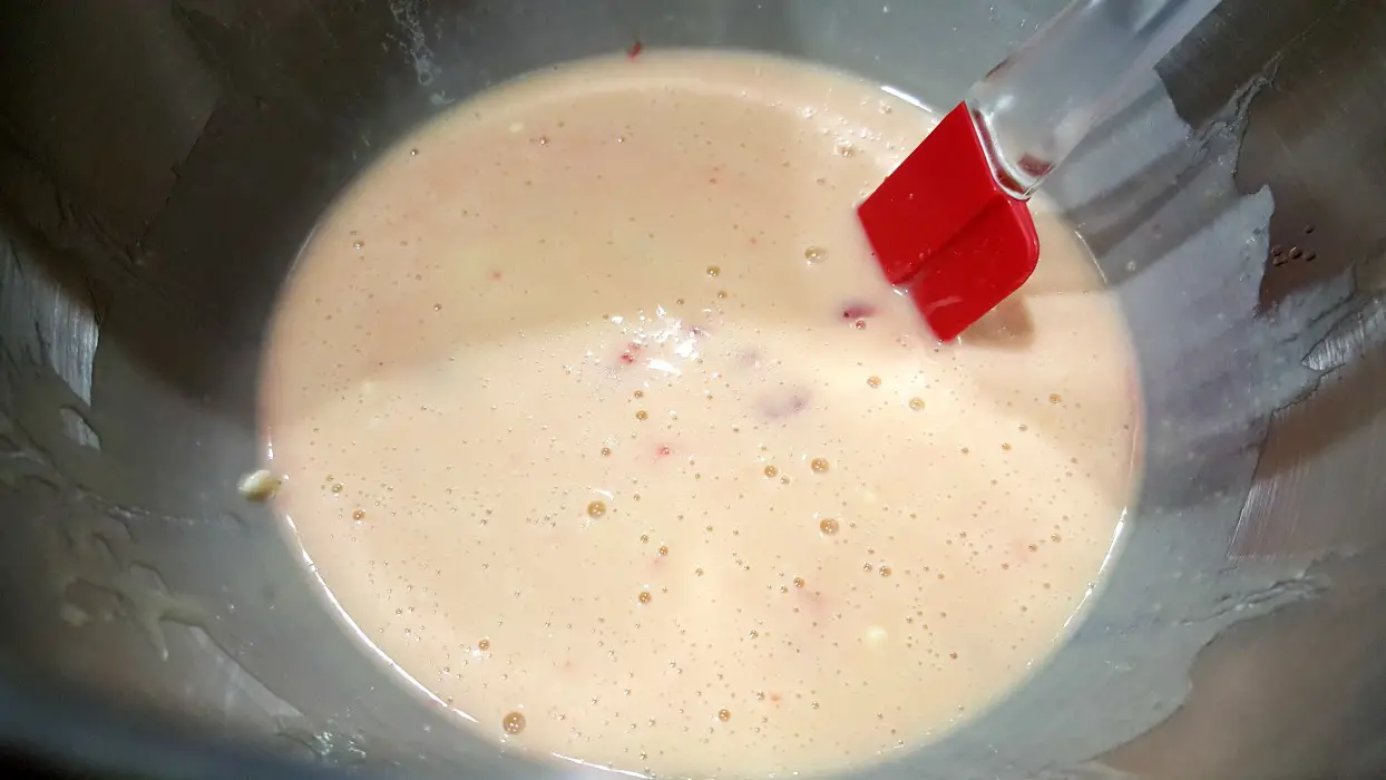 maraschino cheery almond cake batter in a bowl with maraschino cherries mixed in and a red spatula.