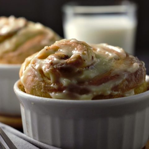 a close up of two cinnamon rolls in ramekins and a glass of milk