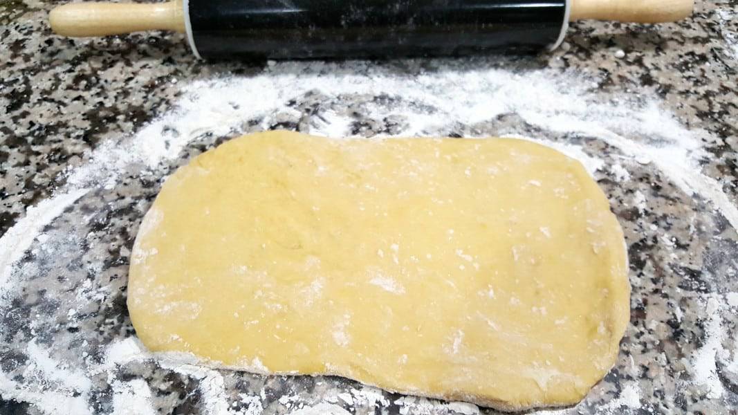 dough rolled out on a floured counter top with a rolling pin.