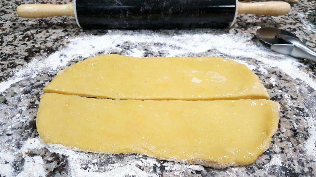 dough rolled out on a floured counter top cut in half and brushed with butter