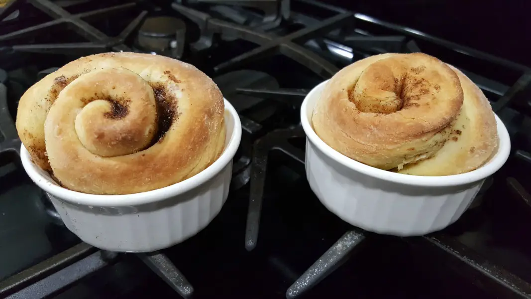 two ramekins filled with baked giant cinnamon rolls on a stove top.