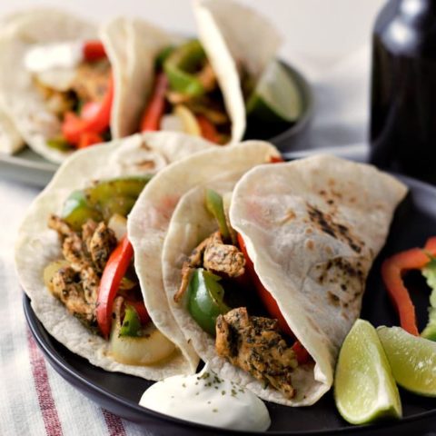 a close up of two plates filled with chicken fajitas and a beer