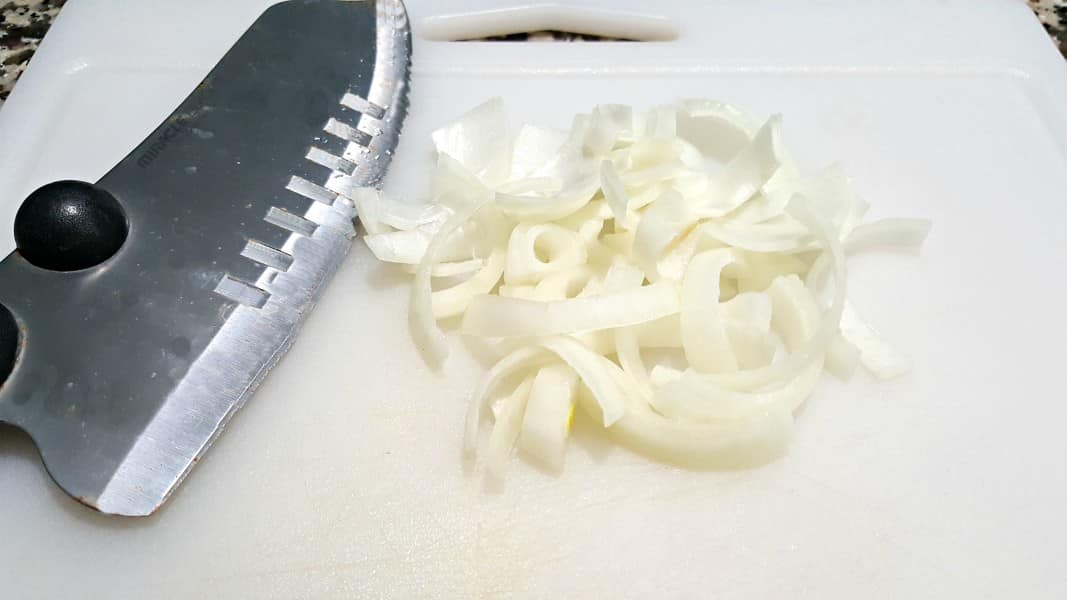 small white onion sliced thing on a cutting board with a chefs knife.