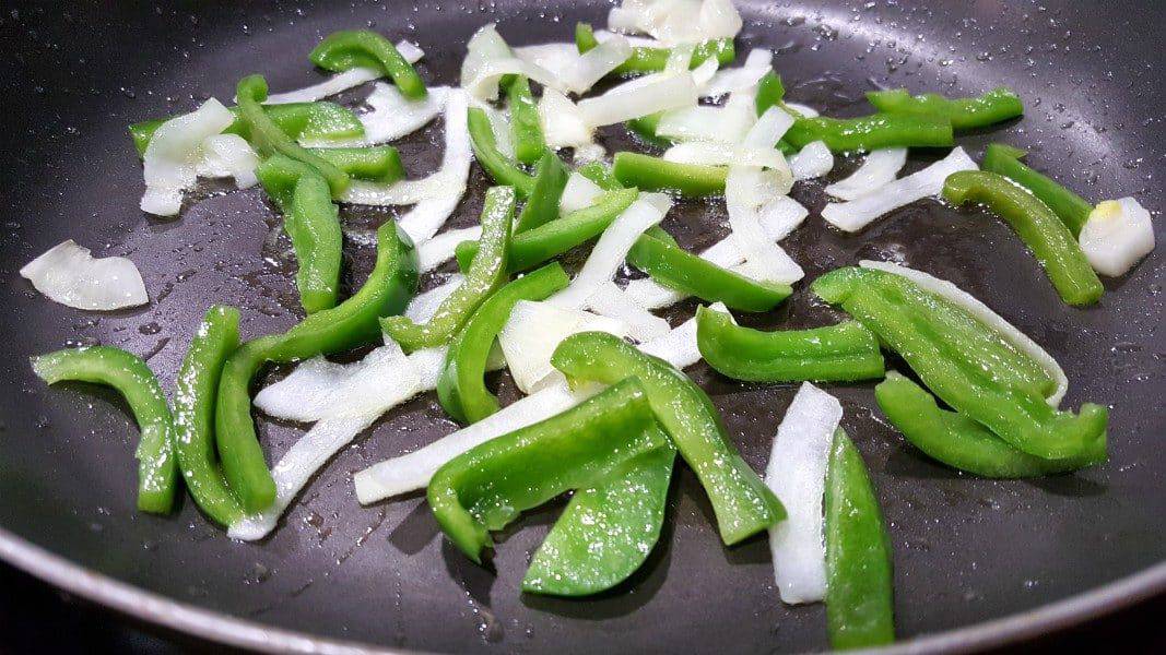 thin sliced onion and green pepper frying in oil in a skillet