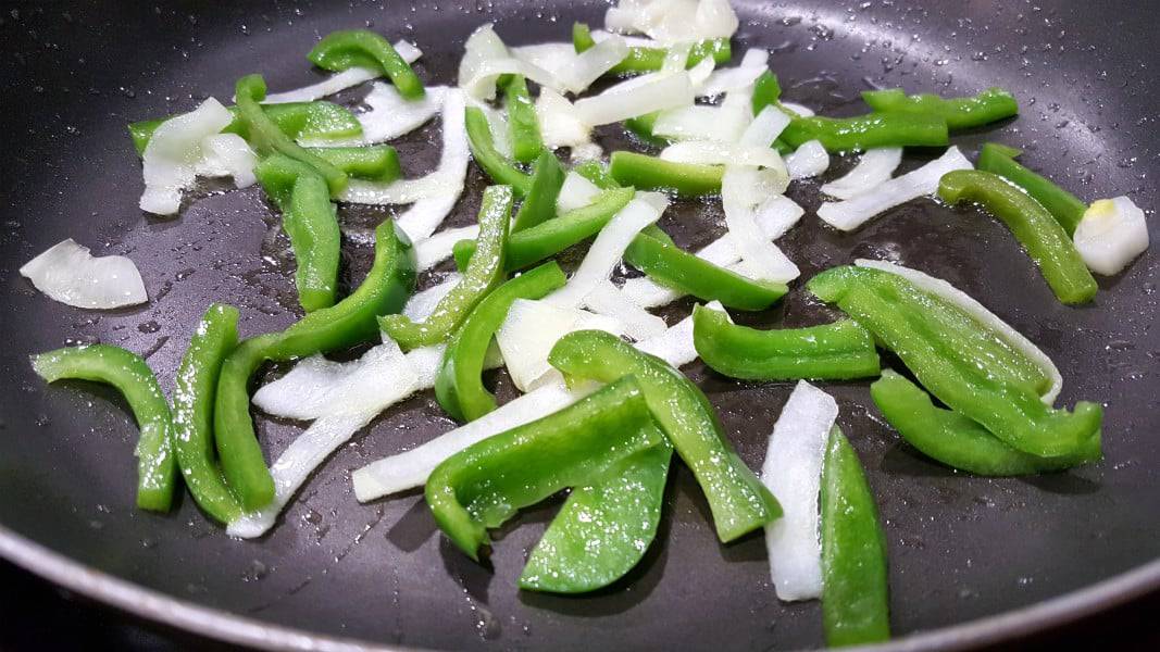 thin sliced onion and green pepper frying in oil in a skillet.