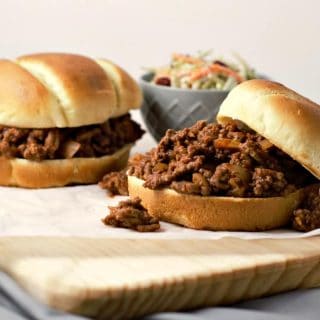 close up of two sloppy joe sandwiches on a cutting board and a bowl of coleslaw