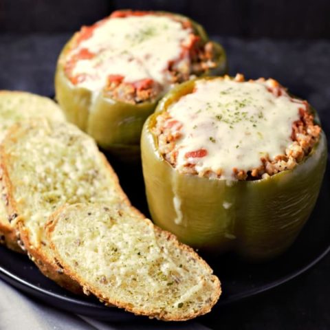 a close up of a plate with three pieces of garlic toast and two green peppers filled with beef and rice topped with red sauce and melted cheese