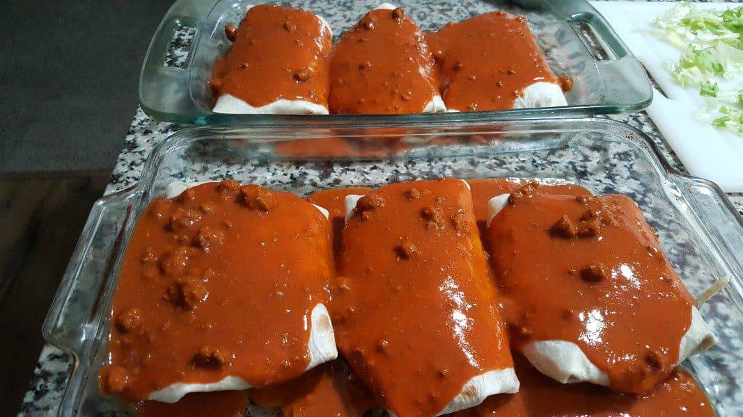 two baking dishes with wet burritos covered in red sauce
