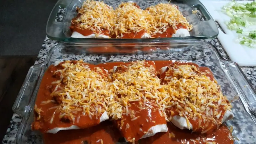 6 wet burritos covered in red sauce and shredded cheese.
