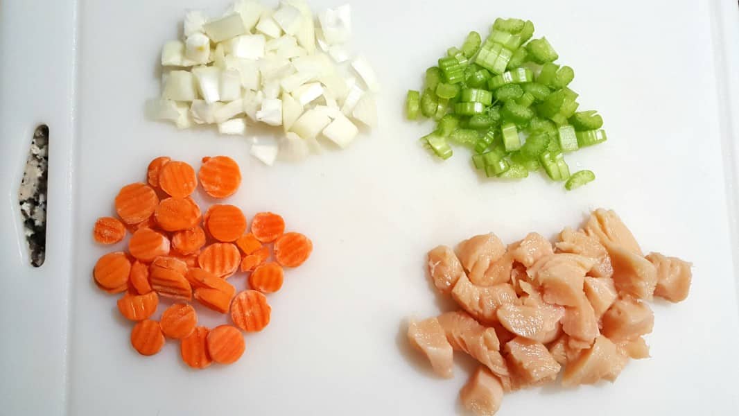 diced onions, diced celery, diced carrots, and diced chicken on a cutting board.