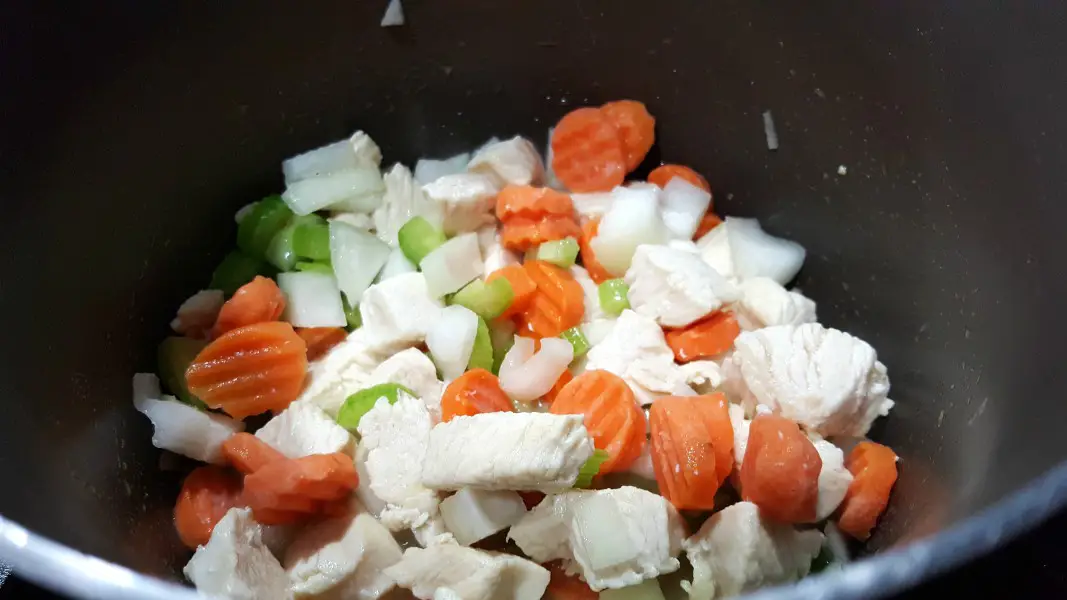 diced onions, carrots, celery, and chicken cooking in a large sauce pan.