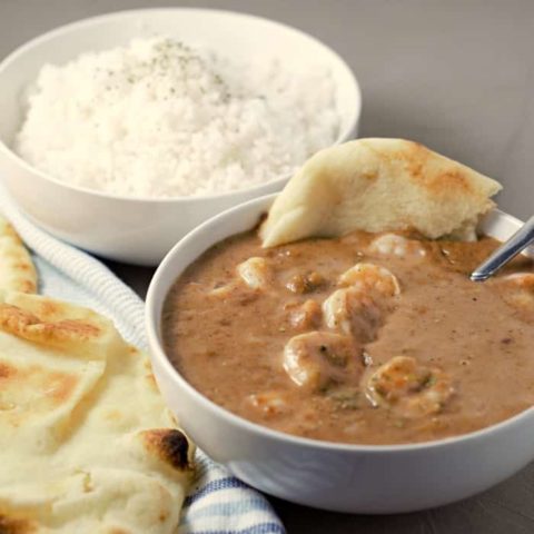 a close up of a bowl of shrimp korma, a bowl of white rice, and a side of naan bread