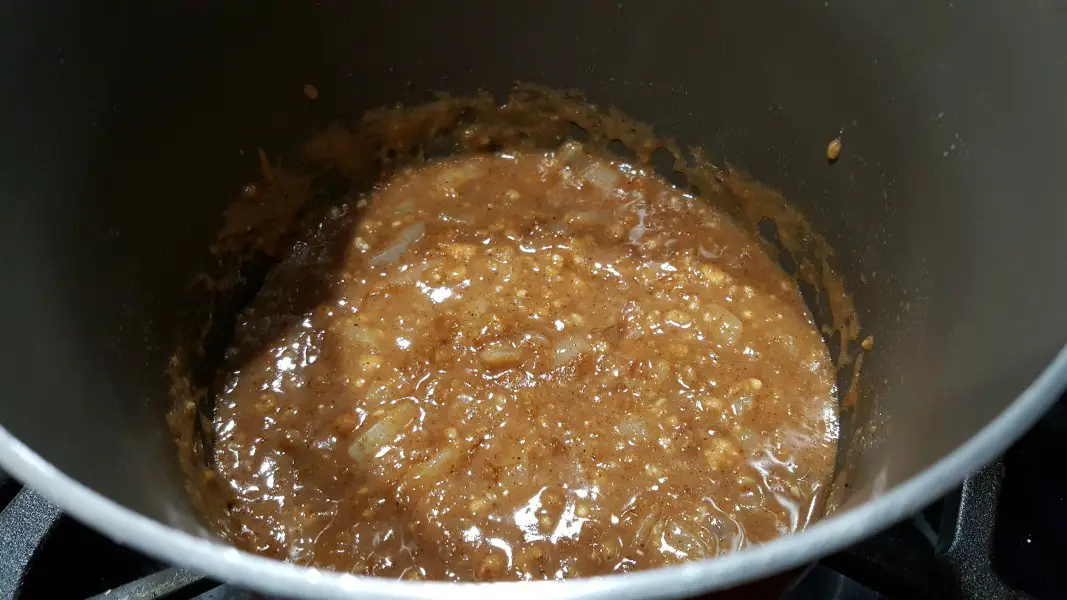 korma sauce ingredients mixed in with chopped onion cooking in a pan.