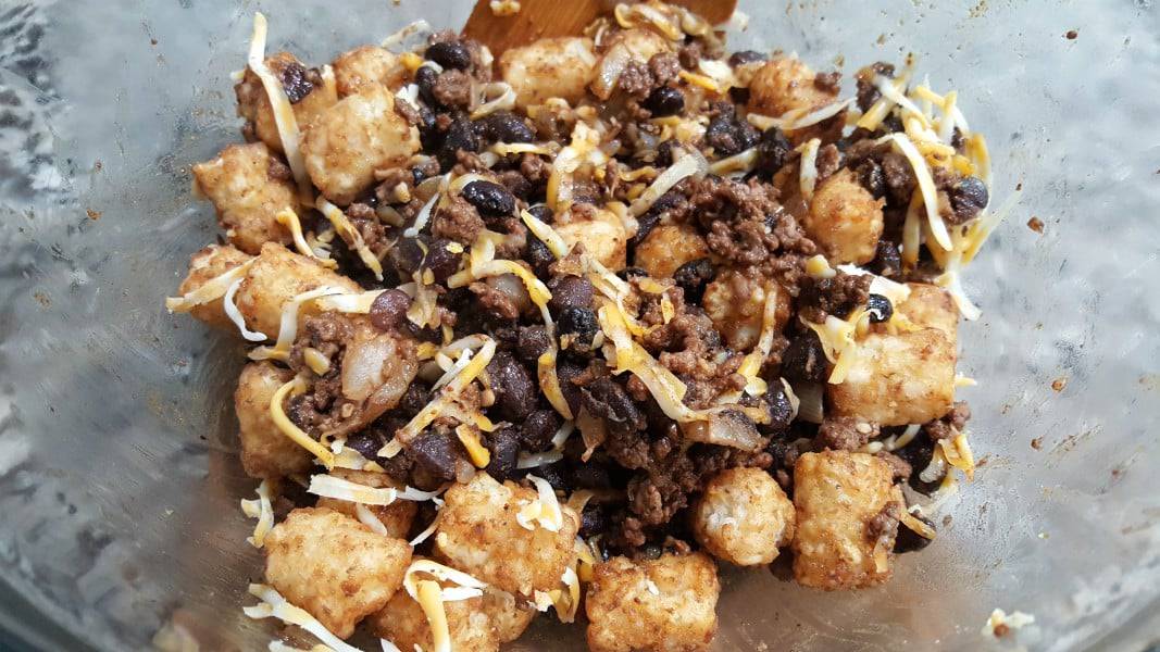 ground beef, black beans, tater tot, and colby jack cheese mixed in a bowl.