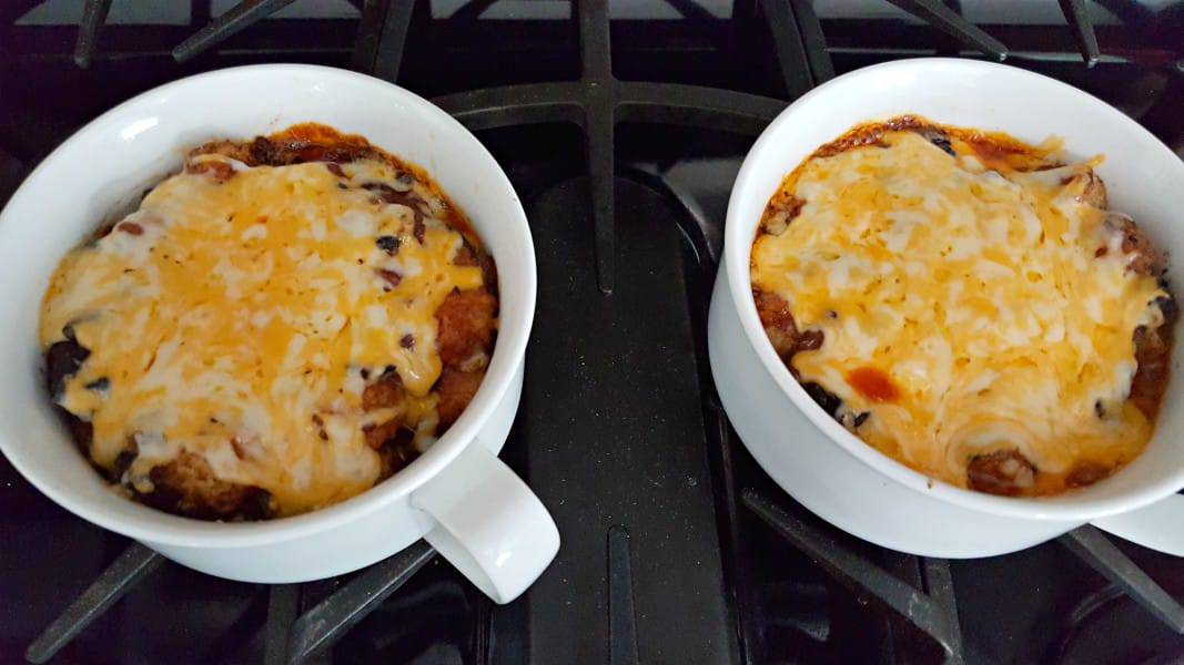 baked taco tater tot casserole topped with melted cheese in two baking dishes.