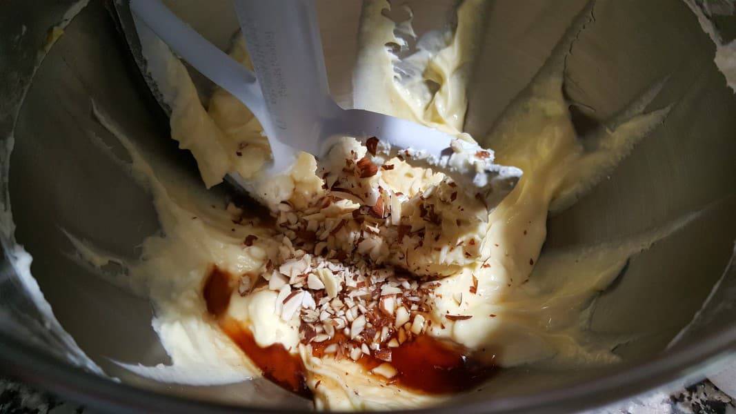 cheesecake filling with chopped almonds and vanilla extract being mixed in a mixer.