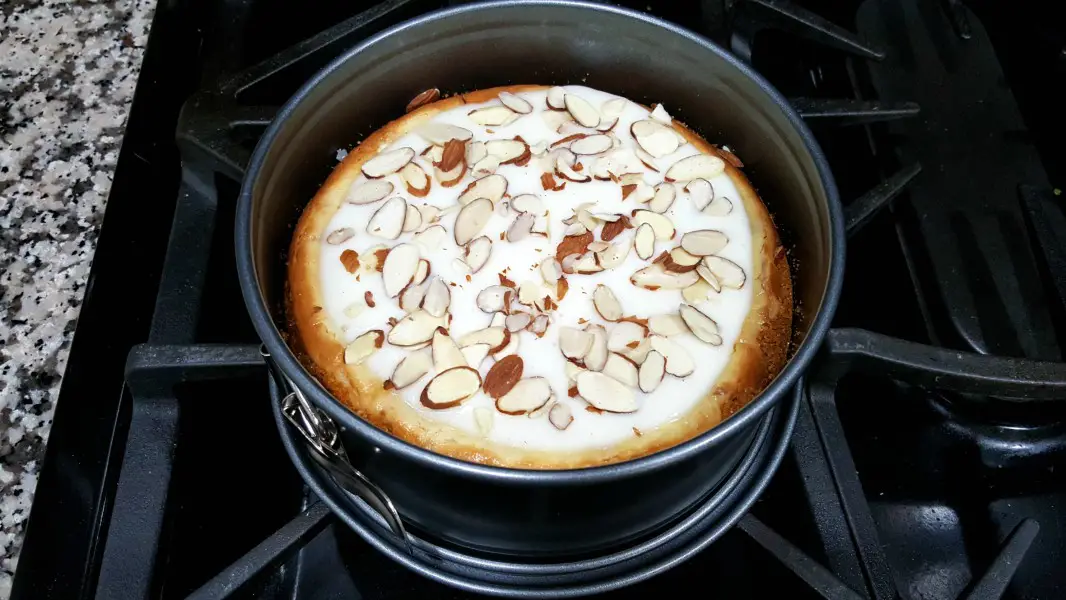 baked White Chocolate Cheesecake topped with sour cream mixture and slice almonds.