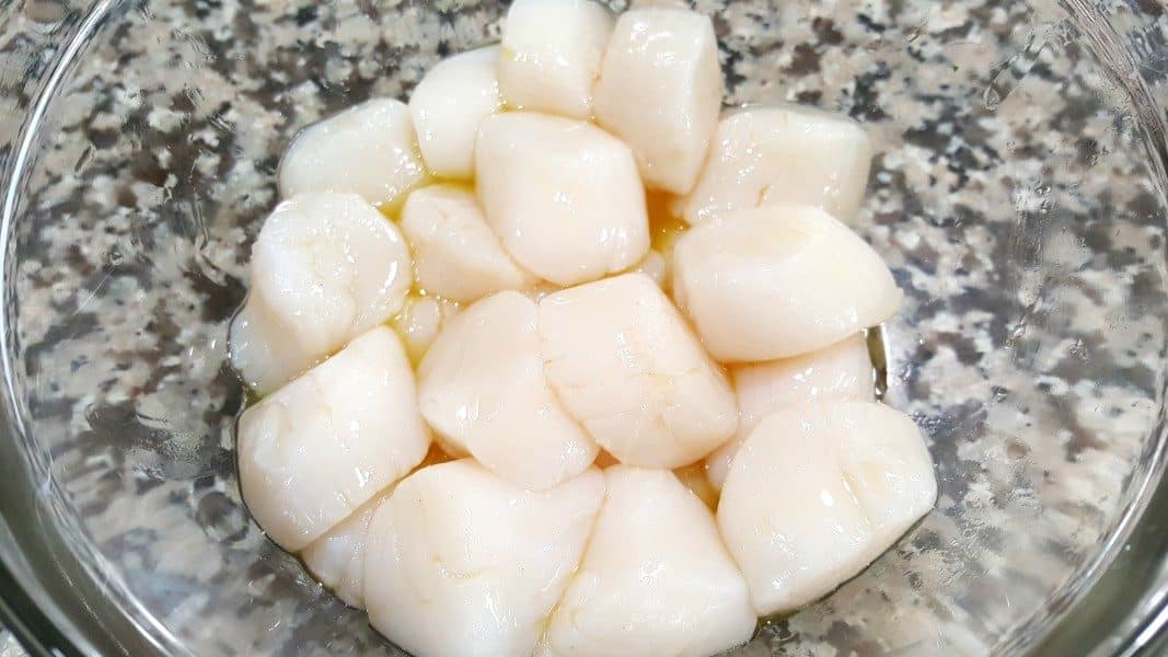 sea scallops mixed with olive oil in a bowl