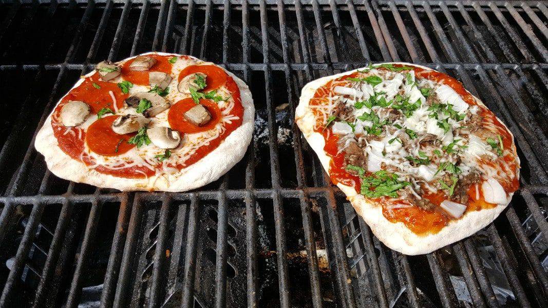 two pizzas cooking on a grill ready to be taken off