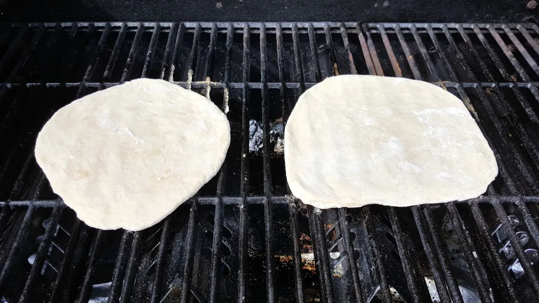 two circles of pizza dough on a gas grill.