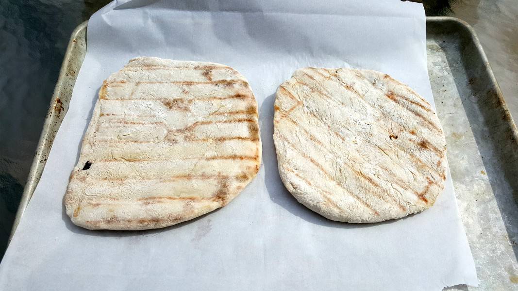 two circles of pizza dough with grill marks on them on a baking sheet.