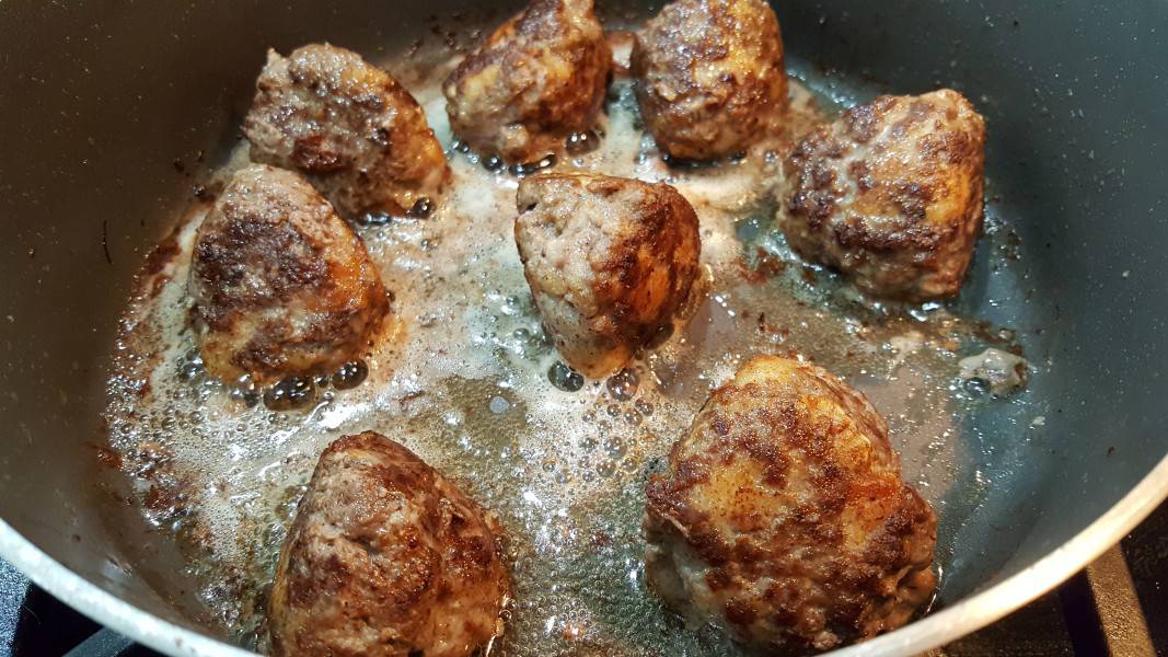 eight Swedish meatballs cooking in a skillet.