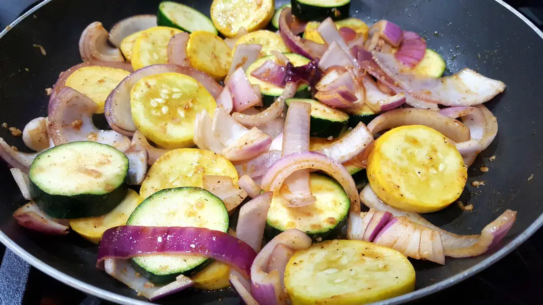 zucchini, yellow squash, and red onion mixed with garlic, olive oil, paprika, salt and pepper cooking in a skillet.