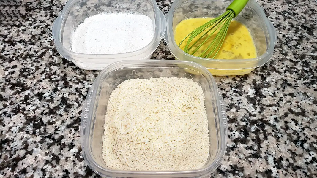 three dishes, first has flour and seasoning mixture, second is egg and water mixture, third is panko and parmesan mixture.