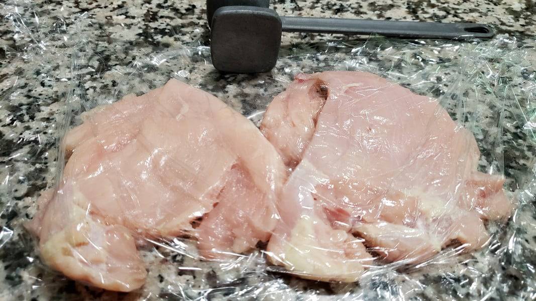 two pieces of chicken pound flat between plastic wrap with meat mallet.