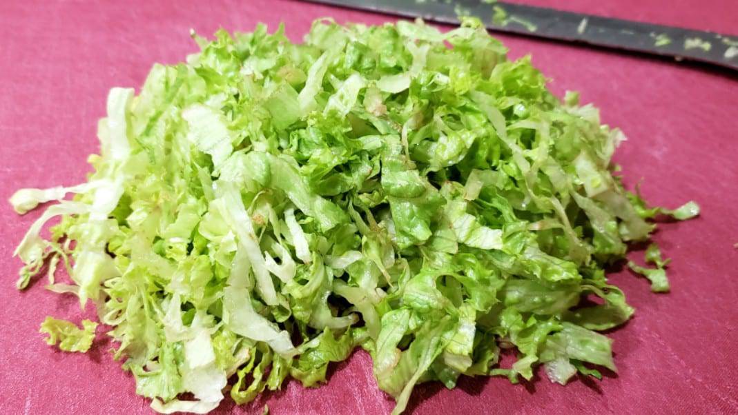 lettuce chopped into shreds on a cutting board with a knife.