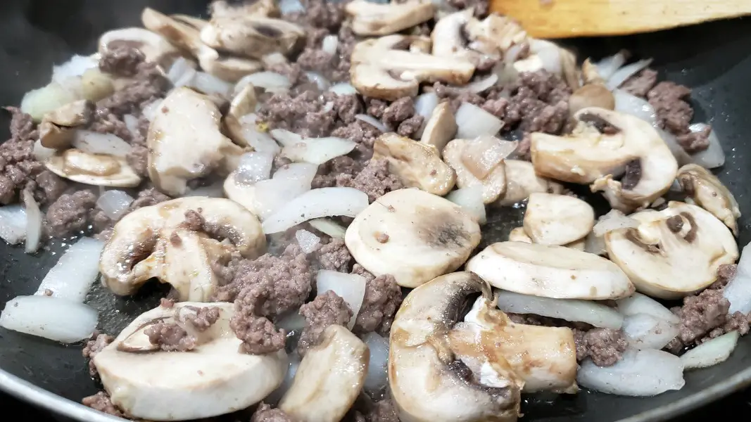ground beef, onions, mushrooms, and garlic cooking in a pan.