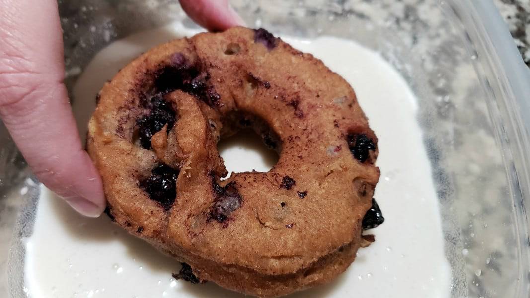 a blueberry donut being dipped into glaze