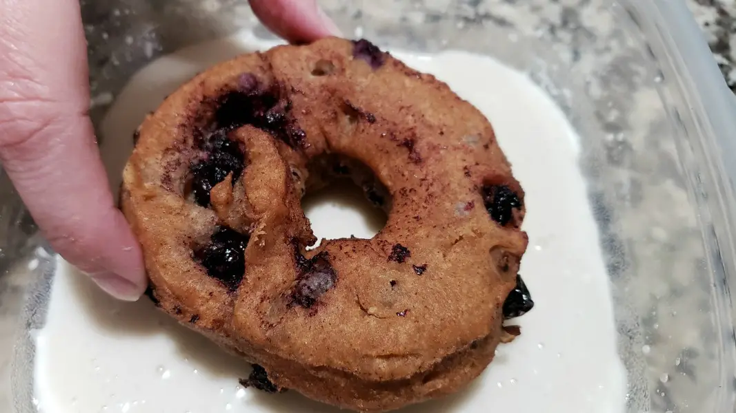 a Blueberry Cake Donut being dipped into glaze.