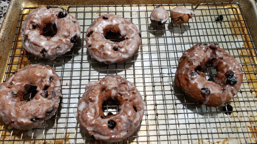 five glazed blueberry donuts and two donut holes on a cooling rack