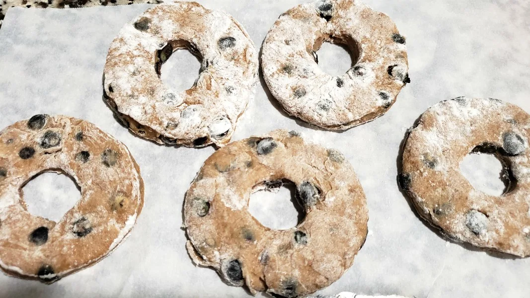 five uncooked blueberry donuts on parchment paper.