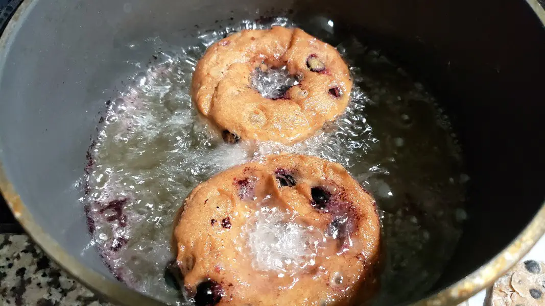 two blueberry donuts frying in a deep fryer.