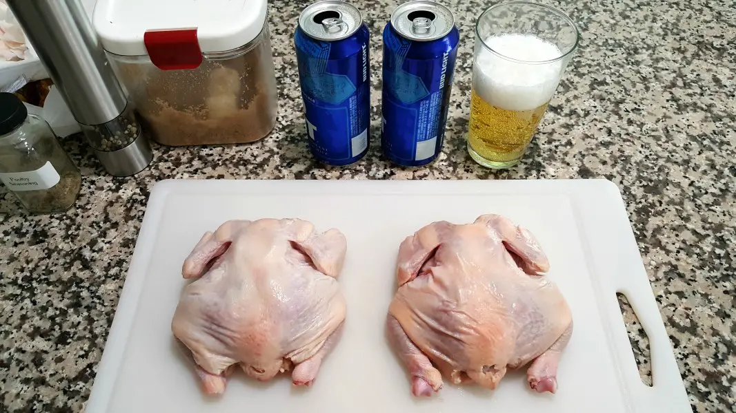 two raw Cornish game hens on a cutting board next to beer cans and seasonings.