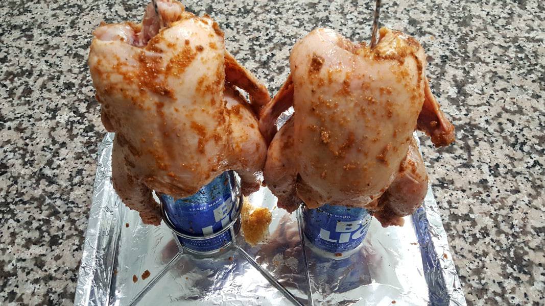 two Cornish hens propped on beer cans ready for grilling.
