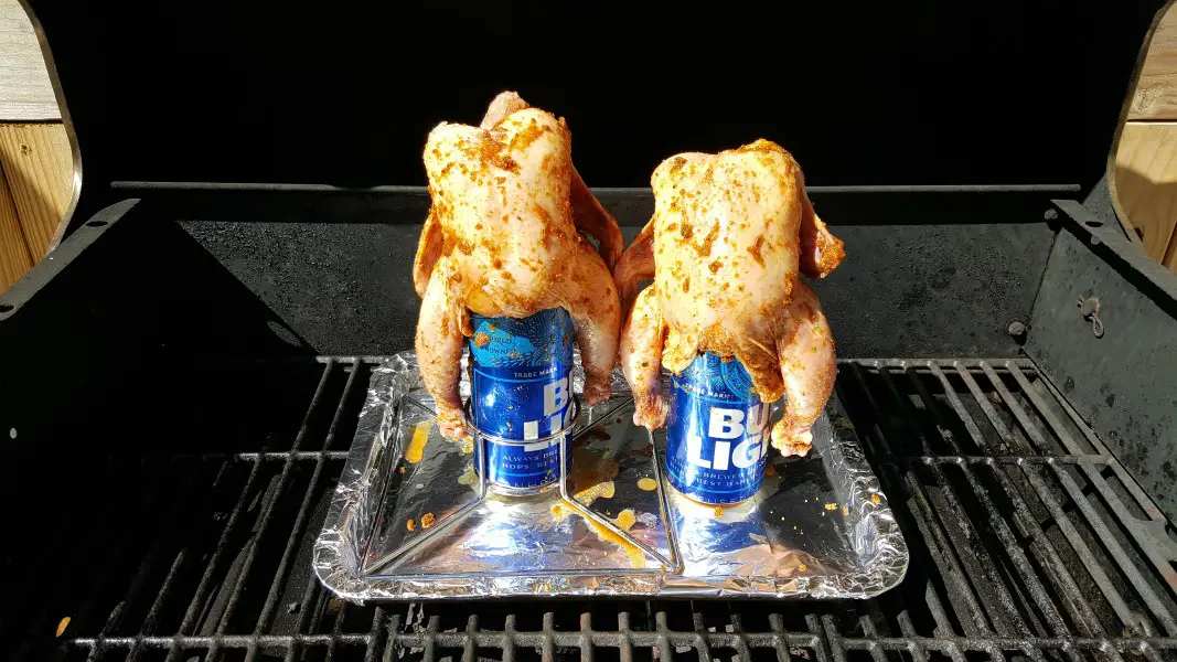 two Cornish game hens on beer cans grilling on a grill.