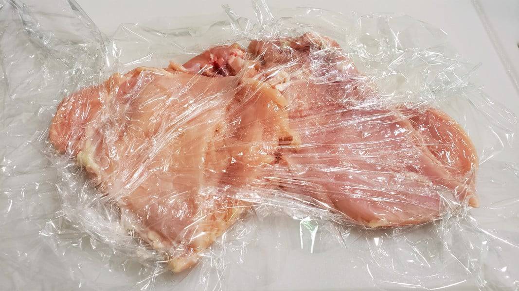 two pieces of chicken pounded flat between plastic wrap