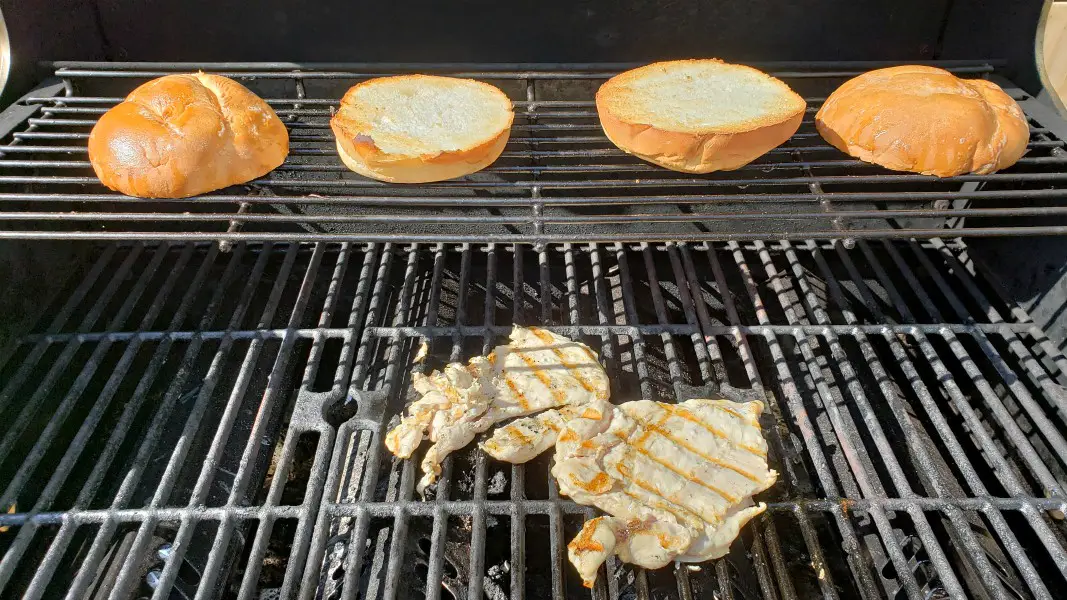 two pieces of chicken grilling and two toasted sandwich buns on the warmer rack