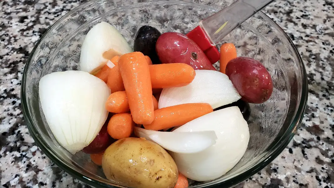 onion, carrots, and potatoes mixed with oil in a bowl.