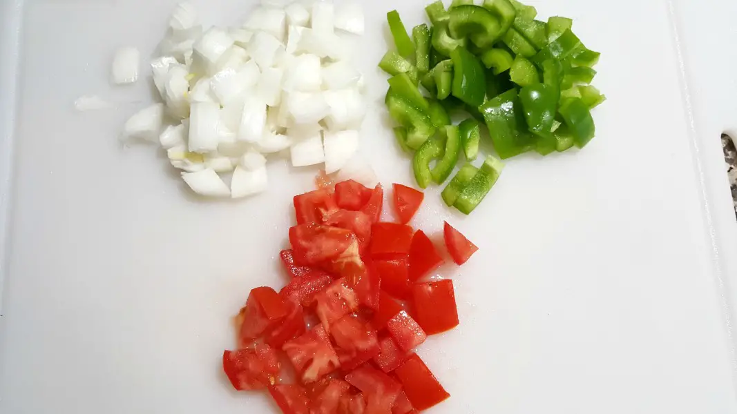 diced onions, green peppers, and tomatoes on a cutting board.