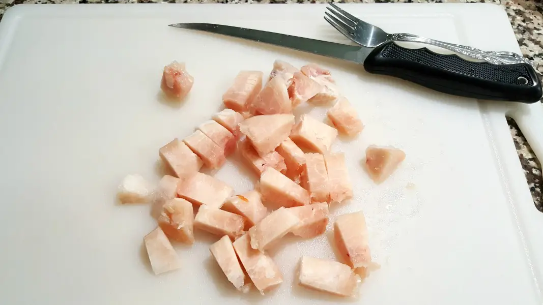 diced chicken on a cutting board with a filet knife and a fork.